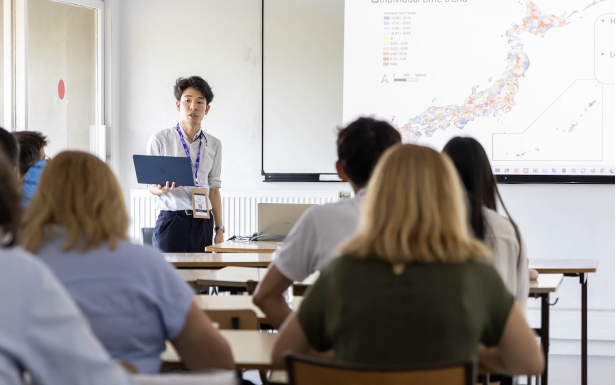 Instructor lecturing to seated students in classroom with a map projected on screen