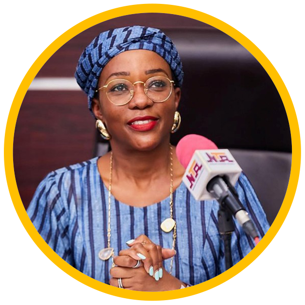 Omotenioye Majekodunmi - Smiling woman with glasses, blue headwrap and striped dress speaking at a microphone